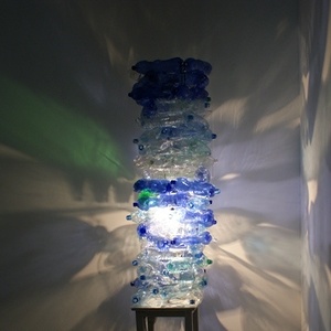 Ein Turm aus gebrauchten Plastikflaschen, die der Künstler auf einer Mülldeponie sammelte, wird durch einen eingebauten Beleuchtungsmechanismus von innen illumiert und durch sich bewegende, monumentale Schatten an der Wand von großer ästhetischer Kra